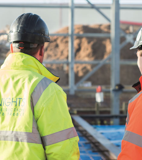 Two individuals in hard hats and safety vests working at a construction site.