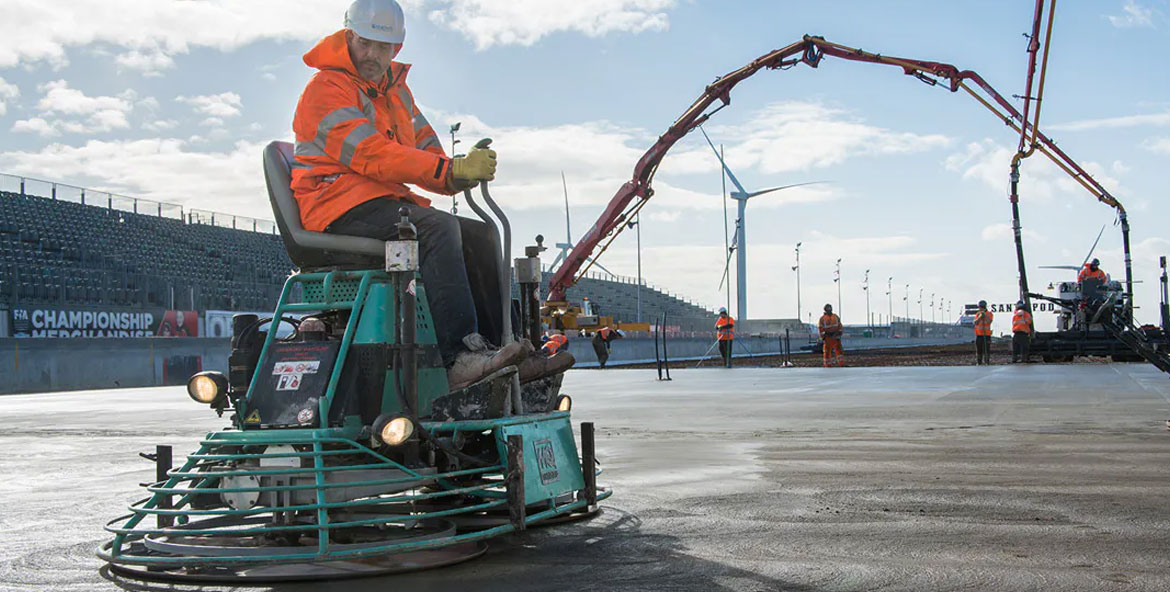 A man in an orange jacket diligently working on a new race track surface.